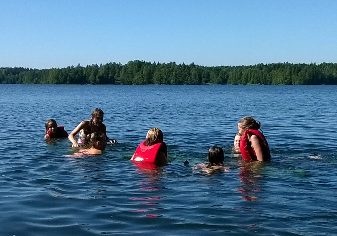 Tytöt uimassa järvessä aurinkoisena päivänä.